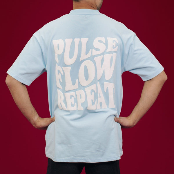 Person wearing a light blue t-shirt with 'PULSE FLOW REPEAT' text on the back against a red background